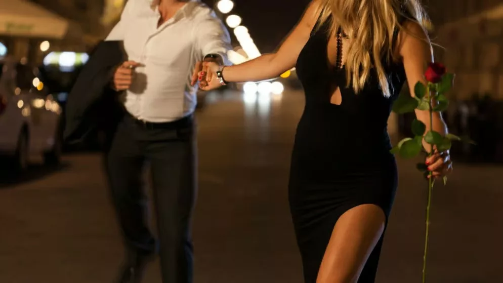 Photo d'un couple qui cours dans la rue, elle est en robe noire et tient une rose à la main