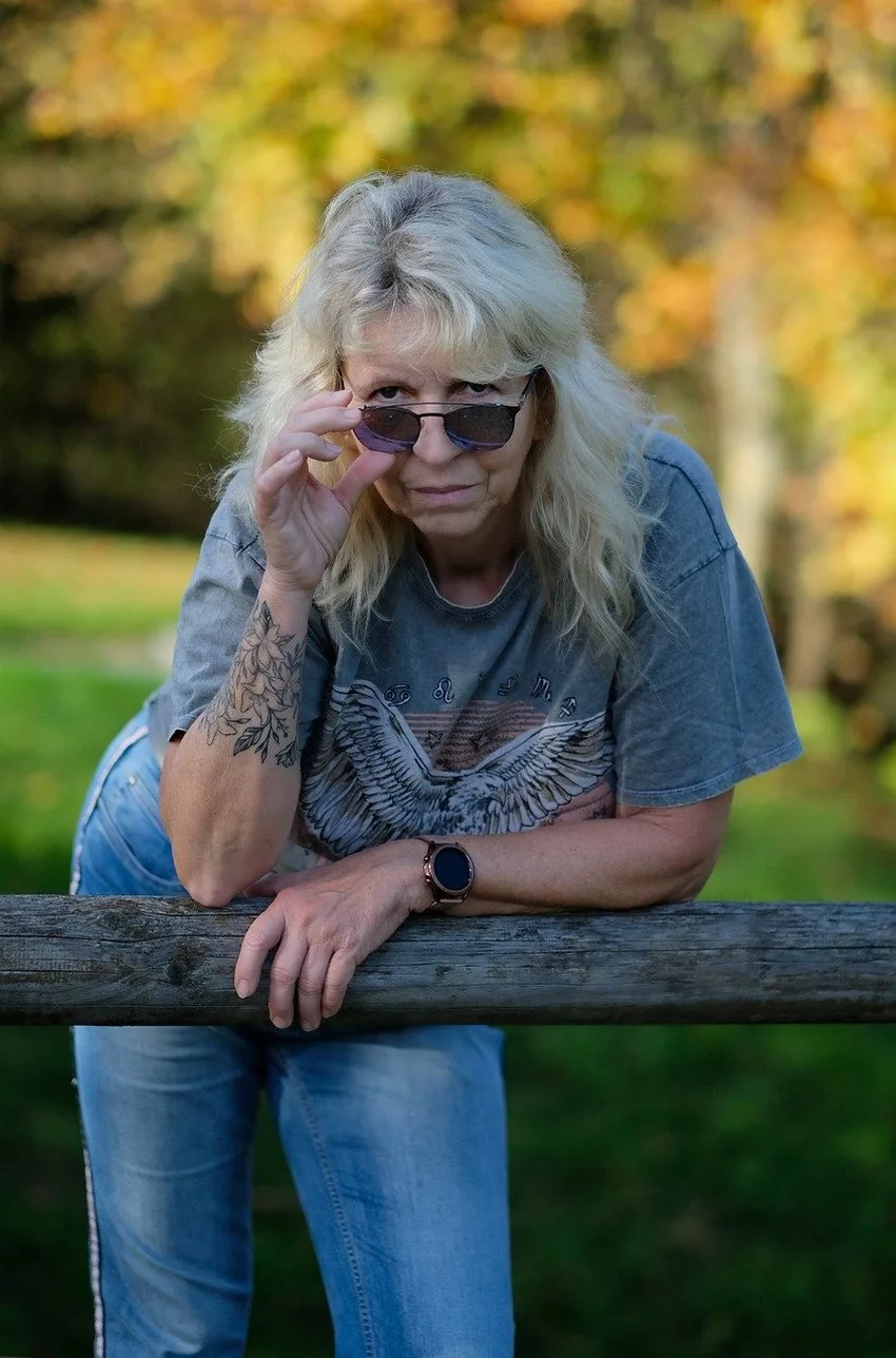 Une femme mature en tee shirt et en jean, cheveux gris baisse ses lunettes de soleil
